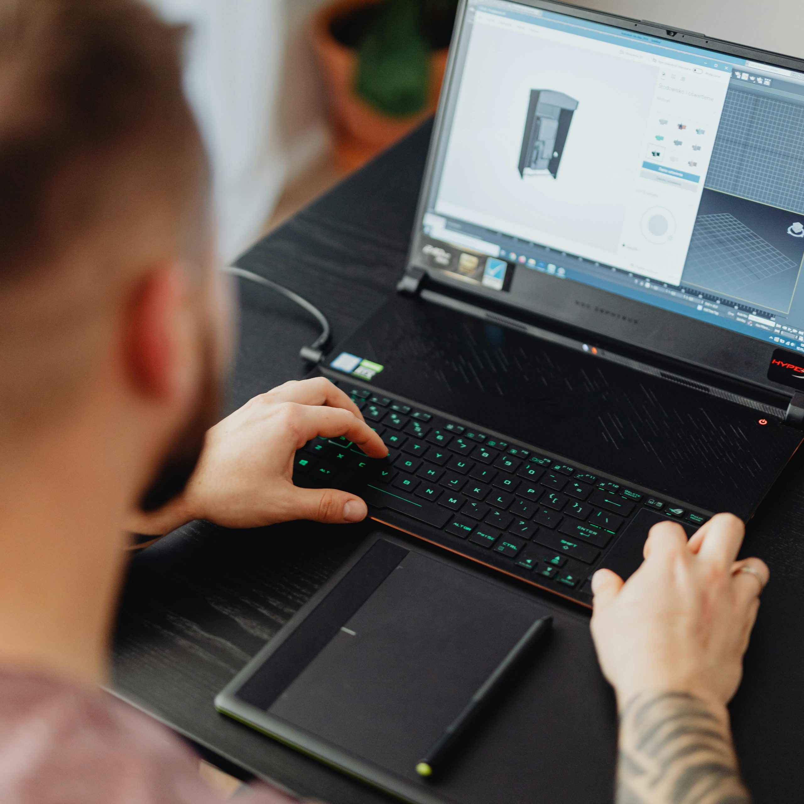 Naše storitve Man using laptop and tablet for 3D design, showcasing modern digital work environment.